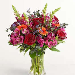 Bouquet of red roses, pink alstroemeria, and orange daisies in a clear glass vase