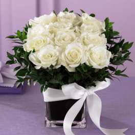 White roses in a square glass vase with a white ribbon