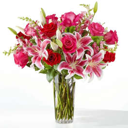 Pink and red roses with lilies in a clear glass vase