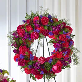 Heart-shaped floral wreath with pink roses and purple flowers on a stand