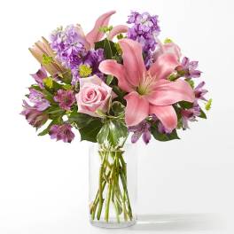 Pink lilies and roses with purple flowers in a clear glass vase