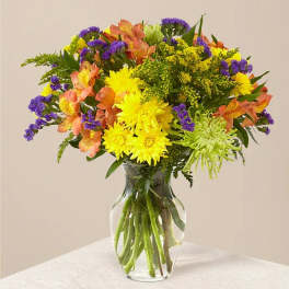 Mixed bouquet of yellow, purple, orange, and green flowers in a clear glass vase