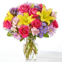 Bouquet of pink roses, yellow lilies, and purple daisies in a clear glass vase