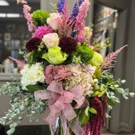 Tall mixed bouquet with pink, purple, white, and green flowers in a glass vase