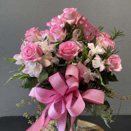 Pink roses and alstroemeria in a glass vase with a large pink ribbon