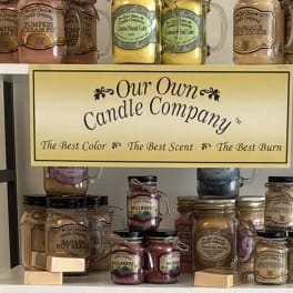 Shelf display of scented candles in mason jars with a company sign.