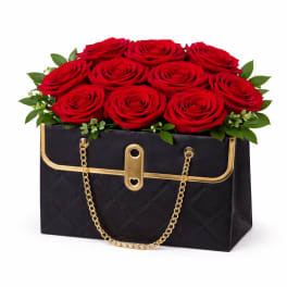 Red roses arranged in a black handbag-shaped box with gold chain handles