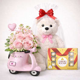 Pink roses in a scooter-shaped vase with a teddy bear and chocolate box