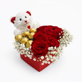 Red roses in a heart-shaped box with a teddy bear and gold chocolates