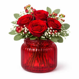 Red roses arranged in a red glass vase with small white filler flowers