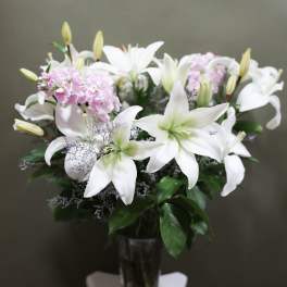 White lilies and pink flowers arranged in a glass vase