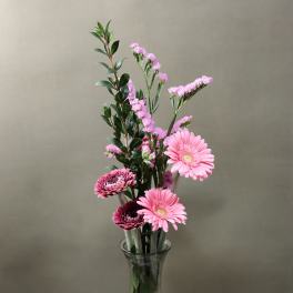 Pink gerbera daisies and small pink filler flowers in a clear glass vase
