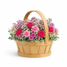 Pink and purple flowers arranged in a wooden basket with a handle