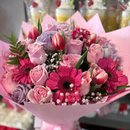 Pink bouquet with roses, gerbera daisies, and tulips wrapped in pastel paper