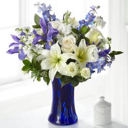 White lilies, roses, and blue-purple flowers in a cobalt vase