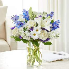 White lilies, roses, and blue flowers in a clear glass vase