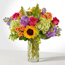Colorful mixed bouquet in a clear glass vase with a sunflower and roses