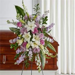 Large floral spray with white lilies, pink roses, and lavender flowers on a casket
