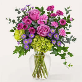 Pink roses and purple flowers in a clear glass vase