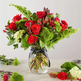 Red roses and green blooms arranged in a clear glass vase with a black ribbon.