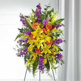 Tall floral standing spray with yellow lilies, orange roses, and purple flowers