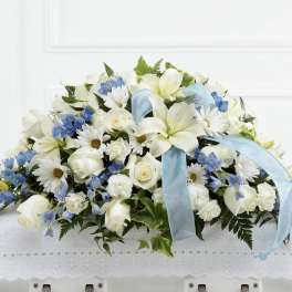 White and blue floral arrangement with a light blue ribbon on a lace-covered base