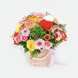 Colorful mixed flower bouquet in a wicker basket with a ribbon