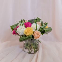 Mixed roses in a clear glass vase with curled green leaves