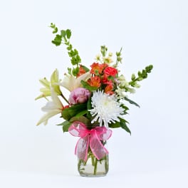 Mixed bouquet of lilies, chrysanthemums, and alstroemeria in a glass vase with a pink ribbon