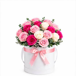 Pink and white roses arranged in a white hat box with a pink ribbon