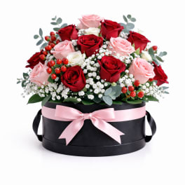 Red and pink roses arranged in a black hat box with a pink ribbon