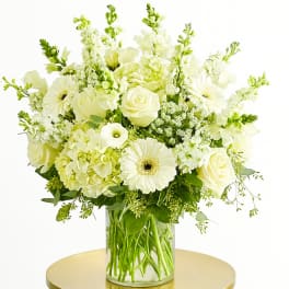 White floral arrangement in a clear glass vase on a gold table
