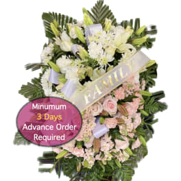 Standing funeral spray with white lilies, pink roses, and a family ribbon