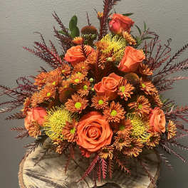Orange roses and chrysanthemums in a low arrangement with burgundy foliage