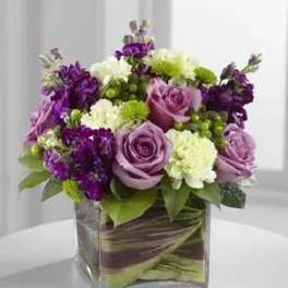Purple and white floral arrangement in a square glass vase