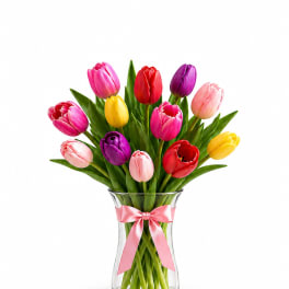 Colorful tulips arranged in a clear glass vase with a pink ribbon