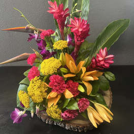 Tropical floral arrangement with pink, yellow, and orange blooms in a wood base