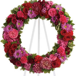 Circular floral wreath on a white easel with red and pink flowers
