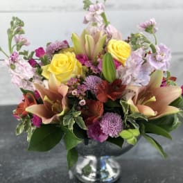 Mixed bouquet of yellow roses, lilies, and pink flowers in a silver vase
