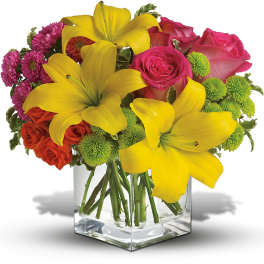 Bouquet of yellow lilies, pink roses, and green button mums in a clear glass vase