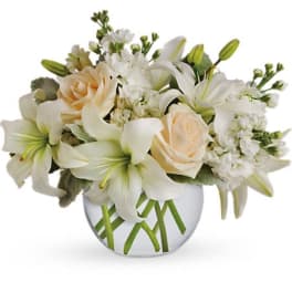 Low arrangement of white lilies and cream roses in a clear round glass vase