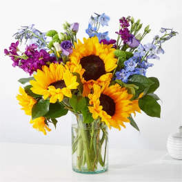 Sunflowers and purple-blue flowers in a clear glass vase
