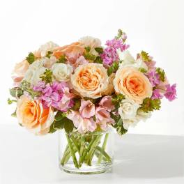 Peach and white roses with pink flowers in a clear glass vase