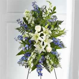 Standing floral spray with white lilies and blue flowers on a black easel