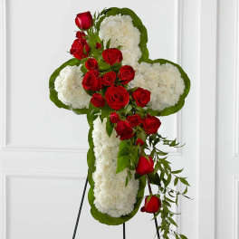 Cross-shaped floral tribute with red roses and white flowers on a stand