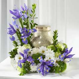 Purple irises and white daisies arranged around a decorative urn
