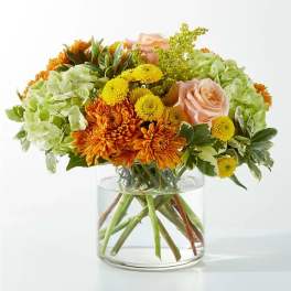 Bouquet of orange and yellow flowers with pale pink roses in a glass vase