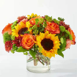 Bouquet of sunflowers, orange roses, and mums in a clear glass vase