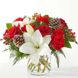 Red roses and white lilies in a clear glass vase with pinecones