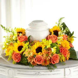 Sunflowers and peach roses arranged around a white urn